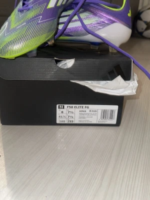 Adidas F50 Elite FG fotbollsskor - Säljer ett par Adidas F50 Elite FG fotbollsskor i lila, limegrönt och vitt. Skorna har en lätt och aerodynamisk design med FG-dobbar för spel på naturgräs. Tillverkade i syntetmaterial för bästa prestanda och passform. Grymma för dig som vill ha speed och kontroll på planen.