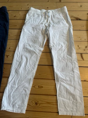 Vita linnebyxor med dragsko från Jack and Jones - Säljer ett par vita linnebyxor med avslappnad passform och resår i midjan samt dragsko från Jack and Jones. Byxorna har raka ben och sidofickor, perfekta för en chill och luftig stil. Materialet är linne som ger en skön känsla och snygg look.