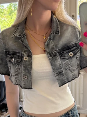 Kort grå jeansjacka med rå kant - Säljer en croppad jeansjacka i tvättad grå färg med rå, fransig kant nertill. Jackan har två bröstfickor med knapp och klassisk krage. Perfekt för dig som vill ha en edgy och trendig look till sommaren.💕💕🌺☀️