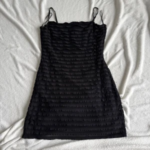 Svart kort klänning från H&M (M) - Säljer en svart kort klänning från H&M med tunna axelband och ett ribbat, strukturerat tyg. Klänningen har en figurnära passform och är perfekt för dig som gillar en enkel men ändå unik look. Materialet känns mjukt och följsamt.