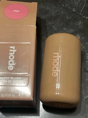 Rhode Pocket Blush Piggy - Rhode Pocket Blush i nyansen Piggy är ett krämrouge i en smidig stickform. Färgen är en mjuk, rosa ton som ger kinderna ett fräscht glow. Förpackningen är beige och kompakt, perfekt att ha med i väskan. Enkel att applicera direkt på huden för en naturlig look.