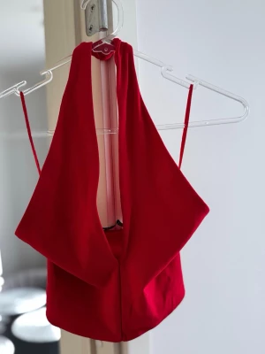 Röd halterneck crop top - Snygg röd halterneck crop top. Toppen har en draperad framsida och är tillverkad i ett mjukt, stretchigt tyg som sitter tajt. Perfekt för att skapa en trendig och ungdomlig look.