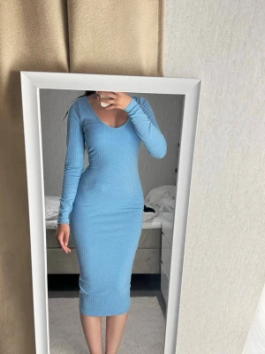 Ljusblå ribbad långklänning - Säljer en ljusblå, ribbad långklänning med lång ärm och djup v-ringning. Klänningen har en tight passform och är tillverkad i ett stretchigt material som framhäver figuren. Perfekt för dig som gillar en enkel men snygg look.
