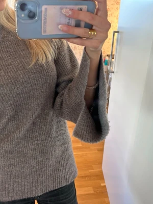 Grå stickad tröja med vida ärmar - Mysig grå stickad tröja med ribbad struktur och vida, trumpetformade ärmar. Tröjan har en avslappnad passform och är perfekt för lager på lager. Passar dig som gillar en trendig och bekväm stil.