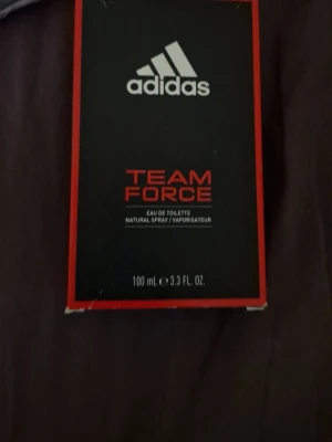 Adidas Team Force Eau de Toilette - Adidas Team Force Eau de Toilette med en intensiv citrusdoft och naturliga eteriska oljor. Flaskan rymmer 100 ml och kommer i en svart och röd kartong med Adidas-loggan och modern design. Perfekt för dig som gillar sportiga och fräscha parfymer.