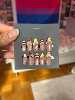 Press-on naglar  - Snygga press-on naglar i mandelform med beige bas, dekorerade med pastellgula och rosa linjer samt söta 3D-kattfigurer. Setet innehåller även:      • 2 självhäftande flikar • 1 nagelfil • 1 nagelbandspinne (träpinne) • 1 Nagellim • 2 alkoholservetter Köpta för 400 kr på Etsy men var för små för mig och gick inte att skicka tillbaka, aldrig använda. 