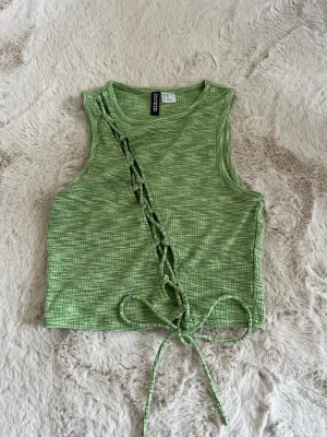 Grön topp  - Säljer en grön ribbad linnetopp från H&M. Toppen har snörning diagonalt framtill och är ärmlös med croppad passform. 