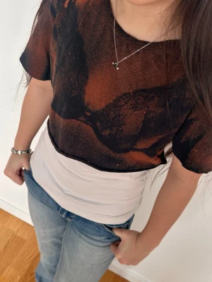 Svart och röd t-shirt med tryck - Cool t-shirt med svart och rött abstrakt tryck som ger en syn av en spets bh. T-shirten har rund halsringning och korta ärmar. Allt är handgjort och blekt.