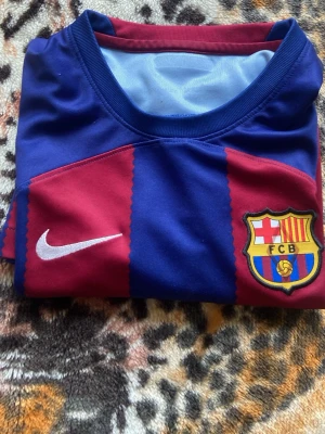 Barcelona matchtröja Nike blå/röd - Säljer en officiell FC Barcelona matchtröja från Nike i klassiska blå och röda vertikala ränder. Tröjan har klubbmärke, Nike-logga och Spotify som sponsortryck på bröstet. Tillverkad i lätt och ventilerande material, perfekt för fotbollsträning eller match.