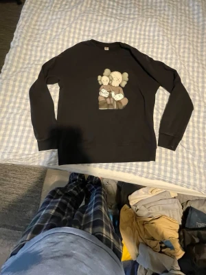 KAWS x Uniqlo svart sweatshirt Storlek 13 - Svart sweatshirt från KAWS x Uniqlo med ett ikoniskt KAWS-tryck framtill. Som man ser på bild 2 så kostar den 60$ på stockx.