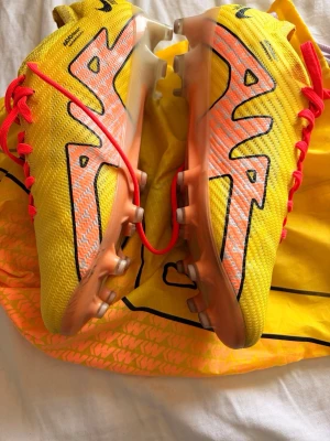 Nike Zoom Mercurial gula fotbollsskor - Säljer ett par Nike Zoom Mercurial fotbollsskor i en riktigt fräsch gul färg med orange och svarta detaljer. Skorna har en lätt och ventilerande ovandel i syntetmaterial och snörning i neonrött. Perfekta för dig som vill sticka ut på planen!