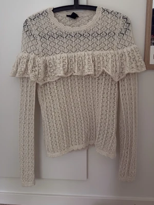 Vit stickad tröja med volang - Supersöt vit stickad tröja med lång ärm och volangdetalj över bröstet och ryggen. Använd fåtal gånger. Perfekt för dig som gillar trendig stil.