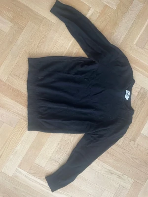 Svart stickad tröja med rund hals - En enkel och stilren svart stickad tröja med rund hals och långa ärmar. Tröjan har ribbade muddar vid ärmslut och nederkant. Perfekt basplagg till garderoben och lätt att matcha med olika outfits. För män och knappt använd.