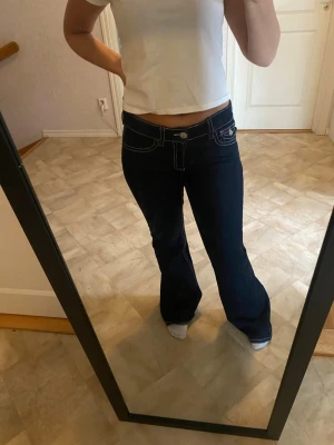 Mörkblå bootcut jeans med kontrastsömmar - Säljer ett par mörkblå bootcut jeans med vita kontrastsömmar och låg midja. 