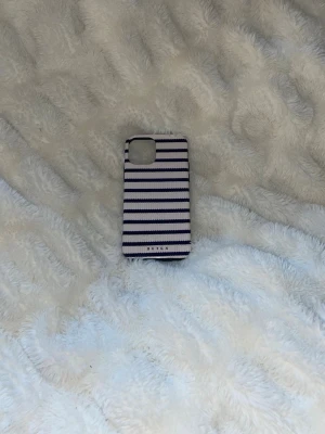 Randigt mobilskal från Burga - Snyggt mobilskal från Burga med vita och mörkblå horisontella ränder. Lite små repor men inget som syns tydligt. Skal till iPhone 12.