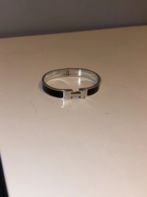 Armband H - Snyggt och stilrent Clic H-armband i silverfärgad metall med svart emalj. Armbandet har den ikoniska H-detaljen.