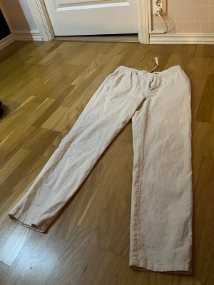 Beiga linnebyxor med dragsko - Les Deux - Snygga beiga linnebyxor med rak passform och elastisk midja med dragsko. Byxorna har två bakfickor med knapp och är tillverkade i ett lätt och luftigt linnetyg. Perfekta för en avslappnad och stilren look.