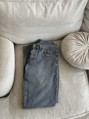 Grå jeans från Dsquared2 - Säljer ett par snygga grå jeans från Dsquared2 med klassisk femficksmodell och raka ben. Jeansen har en diskret logga vid fickan och är tillverkade i mjukt denimtyg som ger en skön passform. Perfekta för dig som gillar stilrena och trendiga plagg.