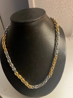 Tvåfärgat kedjehalsband i metall - Snyggt halsband med robust kedjedesign i både silver- och guldfärgad metall. Länkarna är tätt sammanlänkade och ger ett coolt, trendigt intryck. Perfekt accessoar för att lyfta din outfit med en mix av färger och metalliska vibes.