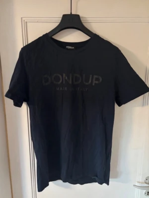 Dondup t shirt - Snygg mörkblå t-shirt från Dondup med diskret logga framtill. Klassisk rund halsringning och korta ärmar. Tillverkad i mjuk bomull för en bekväm känsla. Perfekt till jeans eller shorts för en clean och stilren look.