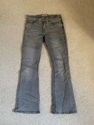 Grå bootcut jeans från Gina Tricot - Säljer ett par gråa bootcut jeans från Gina Tricot. Jeansen har klassisk femficksmodell, normal midja och utsvängda ben. Tillverkade i mjukt denimtyg som ger en skön passform. Perfekta för dig som gillar en retroinspirerad look. Skriv pm vid funderingar!😊