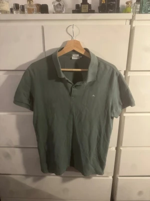 Grön pikétröja från J.Lindeberg - Snygg grön pikétröja från J.Lindeberg i slim fit-modell. Tröjan har klassisk krage, korta ärmar och liten broderad logga på bröstet. Perfekt för en stilren och avslappnad look. Strl L men är bra på en S