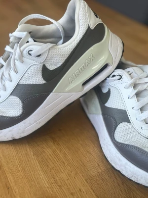 Nike Air Max vita och grå sneakers - Nike Air Max sneakers i vitt och grått med klassisk swoosh-logga på sidan. Ovandelen är i mesh och syntetmaterial för bra andningsförmåga. Tjock sula med synlig Air Max-dämpning och AIRMAX-tryck på sidan. Skön passform och stilren design.