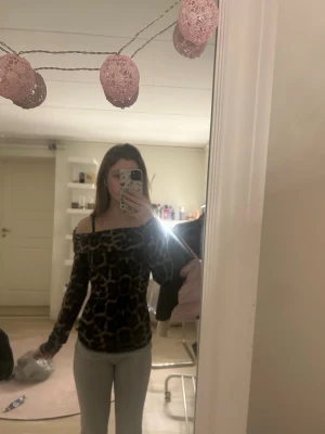 Leopardmönstrad offshoulder topp - Säljer en snygg leopardmönstrad offshoulder topp med lång ärm. Toppens passform är tight och den har en mörk färgton. Perfekt för dig som vill sticka ut och gillar djurmönster.