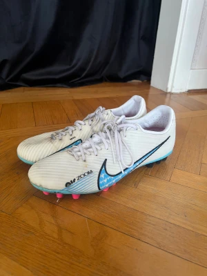 Nike Air Zoom fotbollsskor - Säljer ett par vita Nike Air Zoom fotbollsskor med blå och svarta detaljer samt rosa dobbar skorna är inte tvättade men dem är lite renare än så och dem är i storlek 43 men jag har storlek 41 och dem passar mig men skulle säga att dem passar för folk med storlek 41-42,5 typ (priset går att diskutera) // nytt pris 1 200 kr 🩷