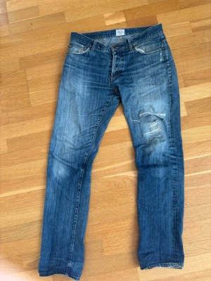 Blå slitna jeans från Denim demon - Säljer ett par blå jeans från denim demon  med snygga slitningar och hål på ena benet. Jeansen har klassisk femficksmodell, normal midja och raka ben. Perfekta för en avslappnad och trendig look.