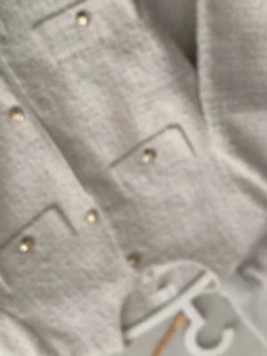 Vit tweed cardigan med guldknappar - Stilren vit cardiganjacka i tweed med rund halsringning och dekorativa guldknappar framtill. Jackan har fyra fickor med lock och en klassisk, rak passform. Perfekt för en chic och trendig look.