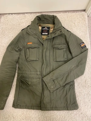 Superdry fieldjacket - Hej! Säljer denna Superdry  fieldjacka i storlek S. Den är varsamt använd och i mycket fint skick, 9/10. Nypris var 2000+, mitt pris 699kr Hör gärna av dig vid minsta fråga eller om du vill ha fler bilder! 🙌 Modellen är 182 och bär S. Passar bra. 