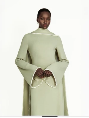 Ljusgrön maxiklänning från Khanum's - Elegant ljusgrön maxiklänning med lång, figurnära siluett och vida ärmar. Klänningen har pärldetaljer längs ärmslut och axlar, vilket ger en unik och lyxig look. Materialet ser ut att vara mjukt och faller snyggt. Perfekt för dig som vill sticka ut. Använt 1 enda gång, nytvättad och i ren skick helt splitter ny.