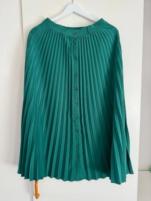 Stradivarius grön midi kjol, storlek S - Plisserad kjol i en vacker grön nyans. Kjolen har knappar framtill som en fin detalj. Den är designad med veck över hela tyget, vilket ger ett elegant fall och rörelse. Midjan är elastisk för en bekväm passform.  Buy shipping label or pick it up from Farsta Centrum in Stockholm.