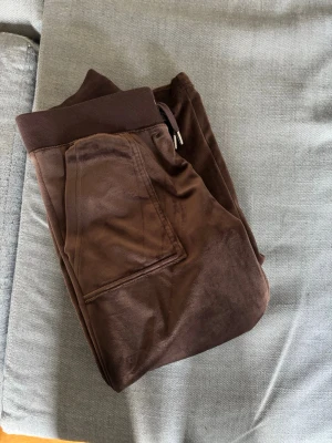 Bruna juicybyxor med fickor - Säljer ett par bruna mjukisbyxor i mjukt velourmaterial. Byxorna har bred resår i midjan och två bakfickor med knappdetaljer. Byxorna är endast använda 1 gång. 