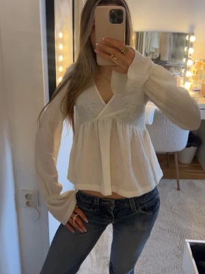 Vit omlottblus med lång ärm - Säljer en vit omlottblus med v-ringning och långärmade puffiga ärmar. Blusen har en luftig och lätt struktur med volang nedtill, perfekt för en trendig look. 💖