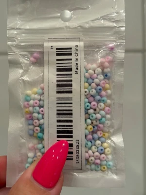 Pastellfärgade pärlor i plastpåse - En liten plastpåse fylld med små, runda pärlor i pastellfärger som rosa, blå, gul, vit och lila. Perfekt för att göra egna smycken eller pysselprojekt. Pärlorna är tillverkade av plast och har ett hål i mitten för enkel trädning. Ca 450 st, 3mm