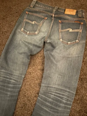 Nudie Jeans Grim Tim ”Dark Nights” (N327) - Nudie  Grim Tim i en väldigt snygg snygg “Dark Nights”-tvätt med tydliga feta fades som ger en riktigt go karaktär. 🧵 Märke & Modell: Grim Tim (Dark Nights, N327) 📏 Storlek & Passform: W28 L32. Slim straight. Den snyggaste och mest eftertraktade nudie modellen.  🧩 Material: 62% Cotton / 38% PBT  📐 Mått.  A: 37,5 cm B: 75 cm C: 101 cm ✅ Skick: 8,5/10 - Riktigt fint skick. Blir bara snyggare desto mer man använder dem.  🧍‍♂️ Referens längder: cirka 178–183 cm.  ‼️ Skickas samma dag eller dagen efter‼️