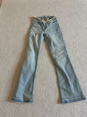 Ljusblå bootcut jeans från nelly - Säljer ett par ljusblå bootcut jeans med klassisk  låg midja. Jeansen har utsvängda ben och är tillverkade i denim. Perfekta för dig som gillar en retrostil och vill ha ett par snygga jeans med avslappnad passform. storleken är 32/short. passar för korta tjejer mellan 150-155cm. Har aldrig använt 