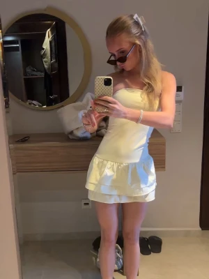 Gul kort klänning - Säljer en snygg gul axelbandslös klänning med volang nertill. Klänningen har en tight passform och är perfekt för dig som vill ha en stilren och fräsch look. 