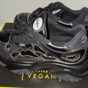Buffalo svarta chunky sneakers - Buffalo sneakers i svart med chunky sula och coola detaljer i grått och silver. Ovandelen har en mix av syntetmaterial och mesh, och skorna är märkta som veganska. Klassisk Buffalo-logga på sidan och plös. Perfekta för dig som gillar streetstyle och statementskor.   Använd 1 gång kort.
