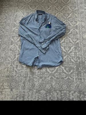 Blårutig skjorta Massimo Dutti - Klassisk blårutig skjorta med lång ärm och knappar framtill. Skjortan har en bröstficka och är tillverkad i ett mjukt bomullstyg. Perfekt för en avslappnad men ändå stilren look.