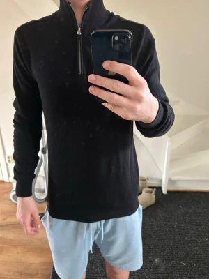 Svart stickad tröja John Henric  - Säljer en svart stickad tröja med hög krage och halv dragkedja framtill från John Henric. Tröjan har långa ärmar och ribbade muddar vid ärmslut och nederkant. Perfekt för lager på lager och enkel att matcha med olika outfits.