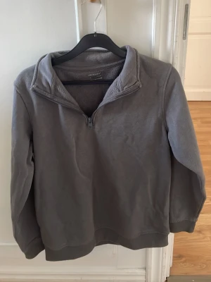 Grå halvzip hoodie från Primark - En stilren grå hoodie från Primark med halv dragkedja framtill och ribbade muddar. Tröjan har en hög krage och är tillverkad i mjukt material, perfekt för en avslappnad look.