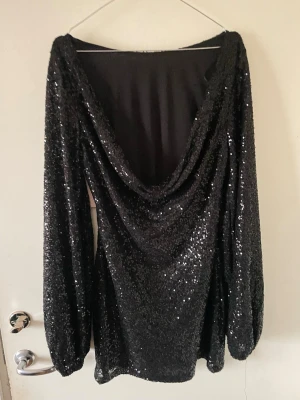 Svart glittrig klänning från Nelly - Svart kort klänning från Nelly med glittriga paljetter över hela tyget. Klänningen har långärmade ärmar och en snygg draperad öppen rygg. Perfekt för dig som vill sticka ut med en festlig look. Nypris: 600, pris kan diskuteras vid snabb affär 