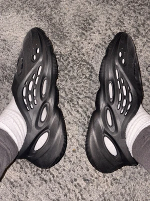 Yeezy foam runners  - Säljer ett par svarta yeezy foam runners med futuristisk design och stora hål för ventilation. Tillverkade i lätt och bekvämt material som formar sig efter foten. Perfekta för chill dagar hemma eller när du vill ha en streetwear vibe.