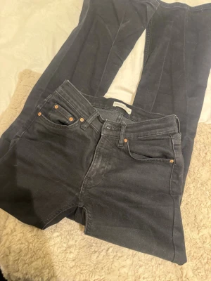 Svarta bootcut jeans med hög midja - Säljer ett par svarta bootcut jeans med hög midja och klassisk femficksdesign. Jeansen har utsvängda ben och snygga kopparfärgade nitar vid fickorna. Perfekta för dig som gillar en retroinspirerad look. Materialet är denim i bomull.