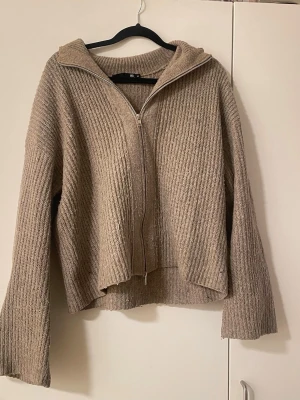 Beige stickad hoodie med dragkedja från lager 157 - Mysig beige stickad hoodie med dragkedja framtill och breda ärmar. Tröjan har en avslappnad passform och ribbstickad struktur. Perfekt för lager-på-lager och chill dagar.