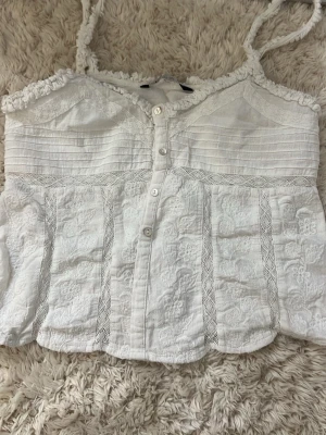 Vit broderad linnetopp från Zara - Supersöt vit linnetopp från Zara med broderade detaljer, knappar framtill och smala axelband. en knapp saknas längst ner.