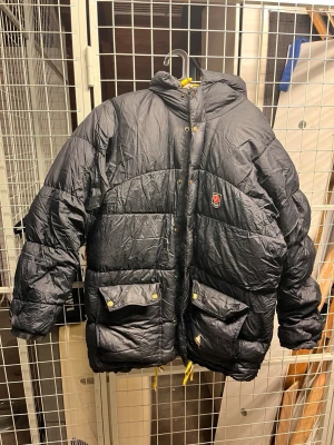 Svart dunjacka från Fjällräven - En äldre Fjällräven jacka som stått på vinden och dammat. Har ej använts på några år så kemtvätt kan behövas. Se bilder för skavanker. Storlek S